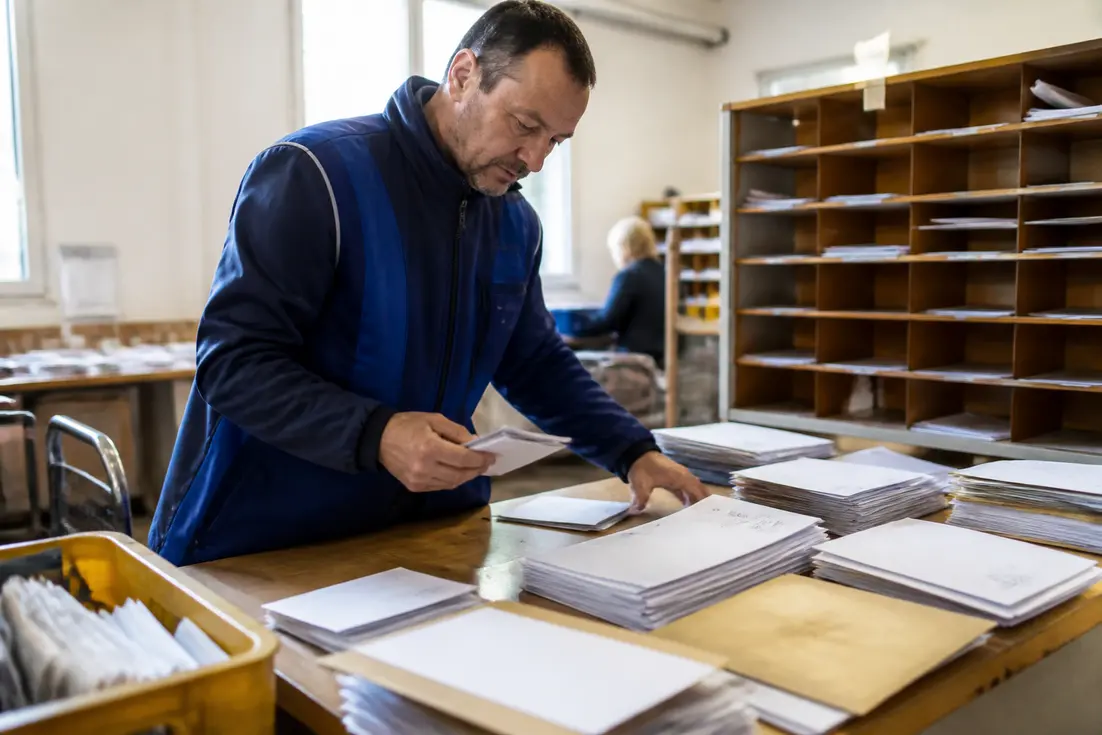 Un facteur classe le courrier dans un bureau lumineux en Normandie avec son Bayeux code postal.