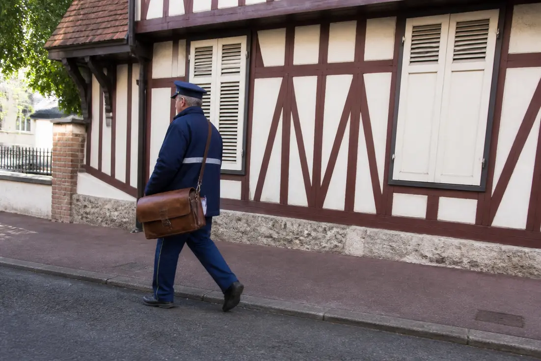 facteur en uniforme marchant dans une rue normande avec cabourg code postal