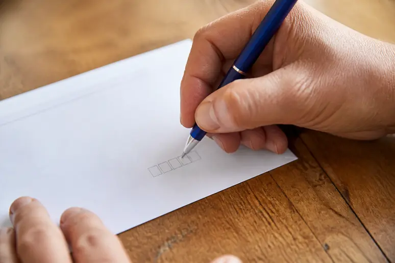 Main écrivant un code postal sur une enveloppe pour éviter les erreurs fréquentes lors de l'adressage.