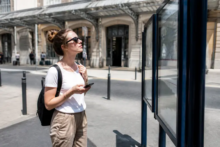 Femme consultant un panneau d'affichage de bus devant la gare de Trouville-Deauville