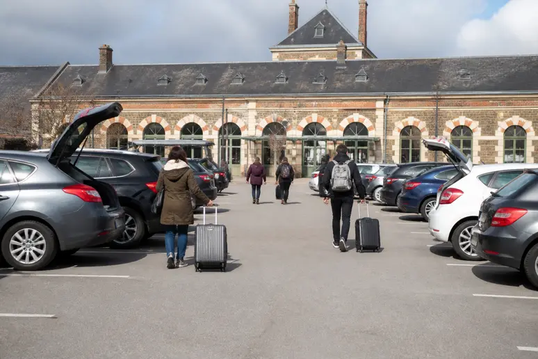 Parking devant la gare Pontorson Mont-Saint-Michel, avec des voyageurs rejoignant la station.