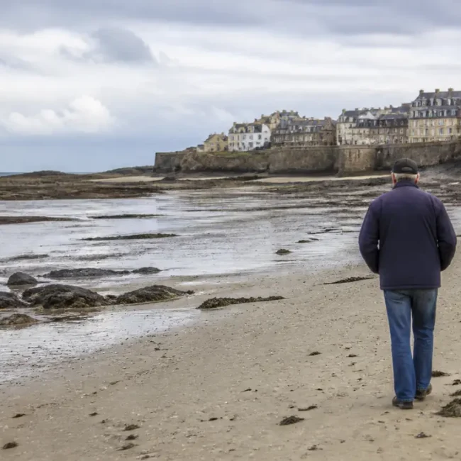 Un promeneur découvre l'estran rocheux lors de la marée basse à Granville en Normandie.