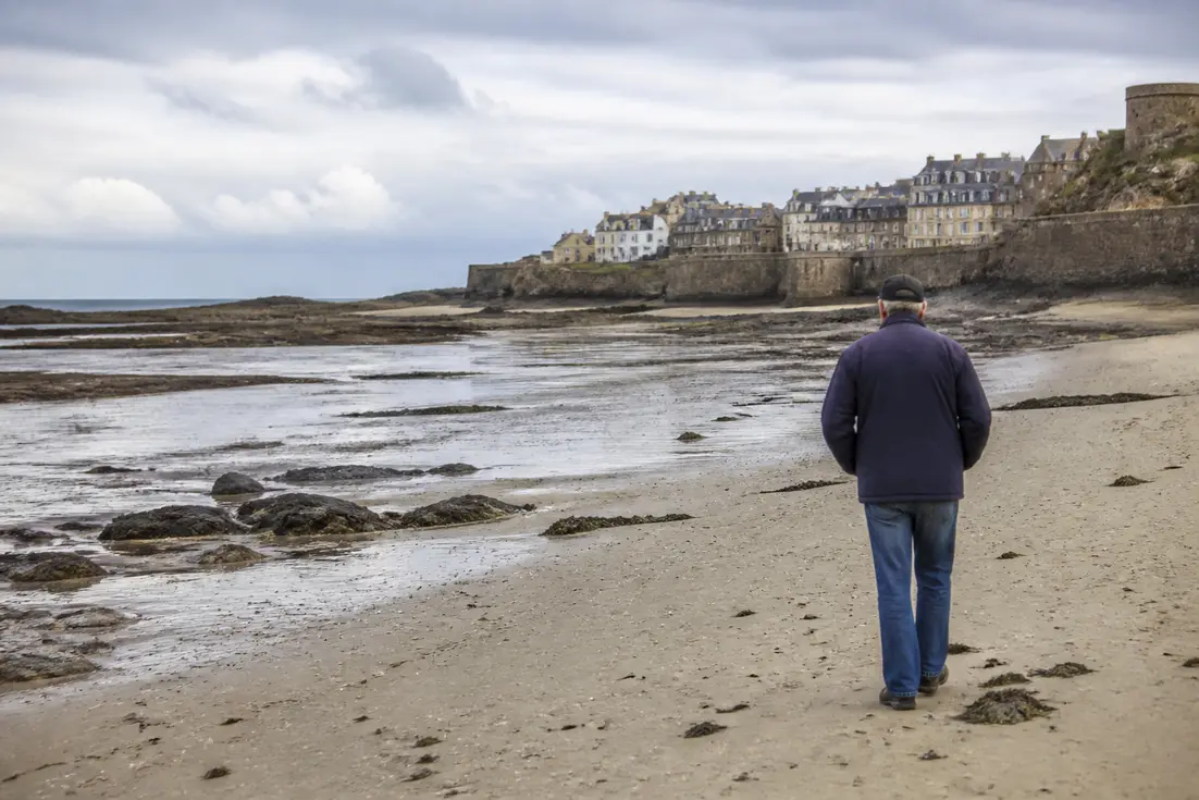 Un promeneur découvre l'estran rocheux lors de la marée basse à Granville en Normandie.