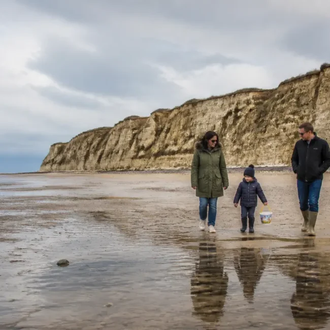 Une famille marche sur la plage au pied des falaises de Houlgate en consultant un horaire des marées Houlgate