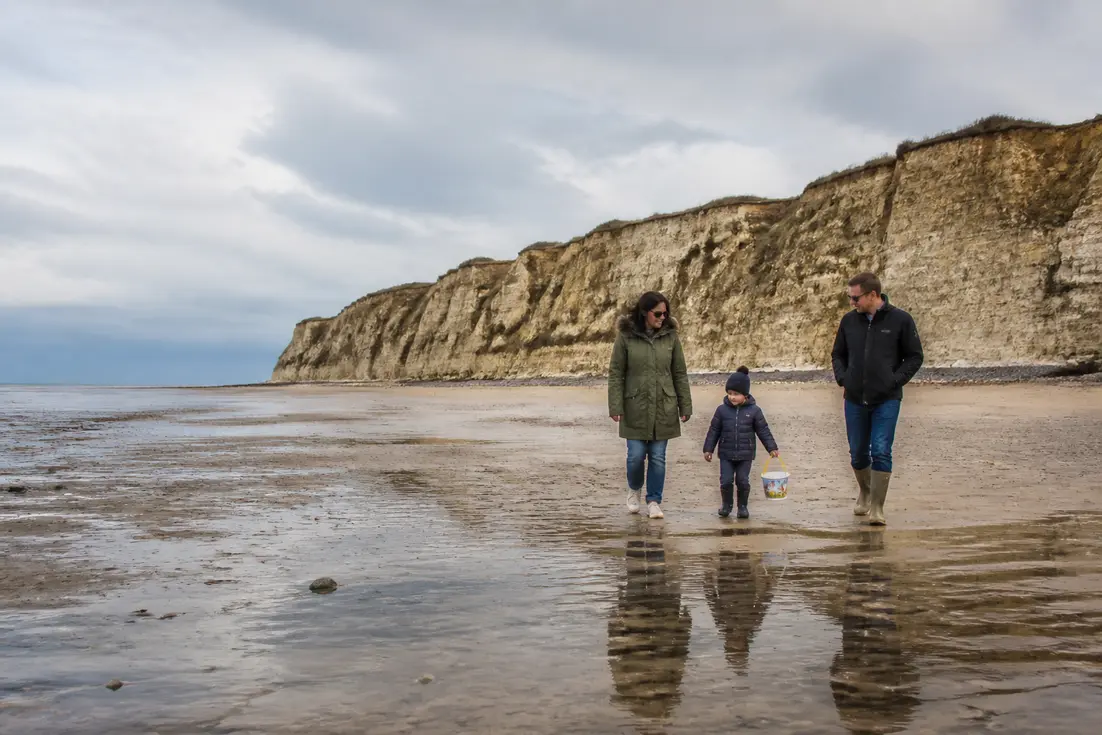 Une famille marche sur la plage au pied des falaises de Houlgate en consultant un horaire des marées Houlgate