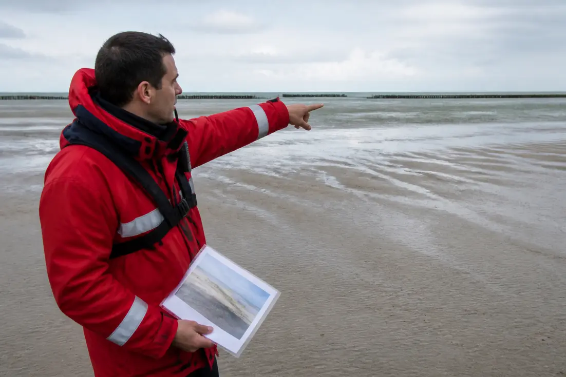 Un agent de sécurité côtière sur le sable humide explique la maree deauville à marée basse.
