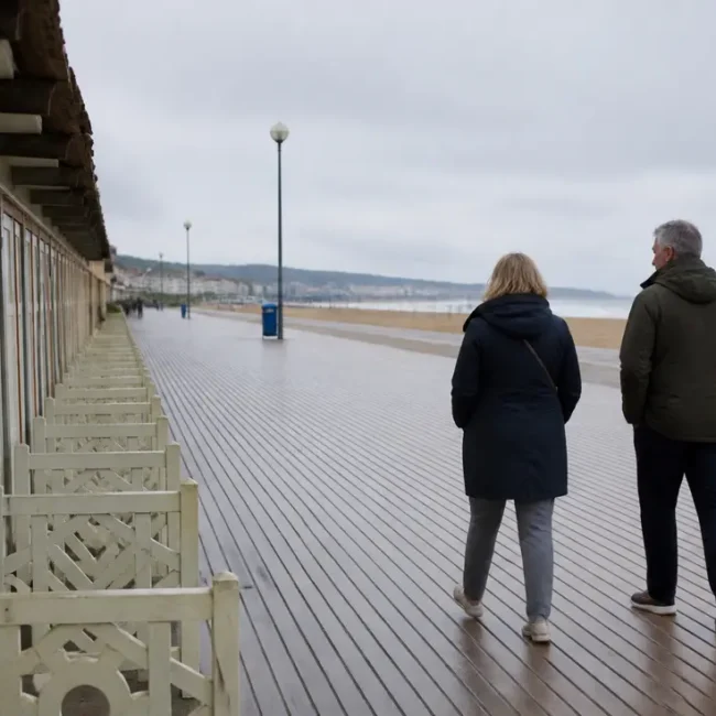 Couple en veste marchant sur les planches de la plage, idée de que faire à Trouville-sur-Mer ce week-end.