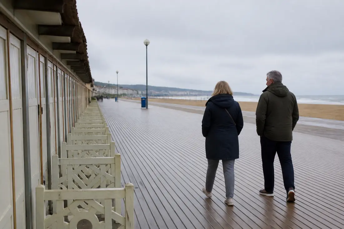 Couple en veste marchant sur les planches de la plage, idée de que faire à Trouville-sur-Mer ce week-end.