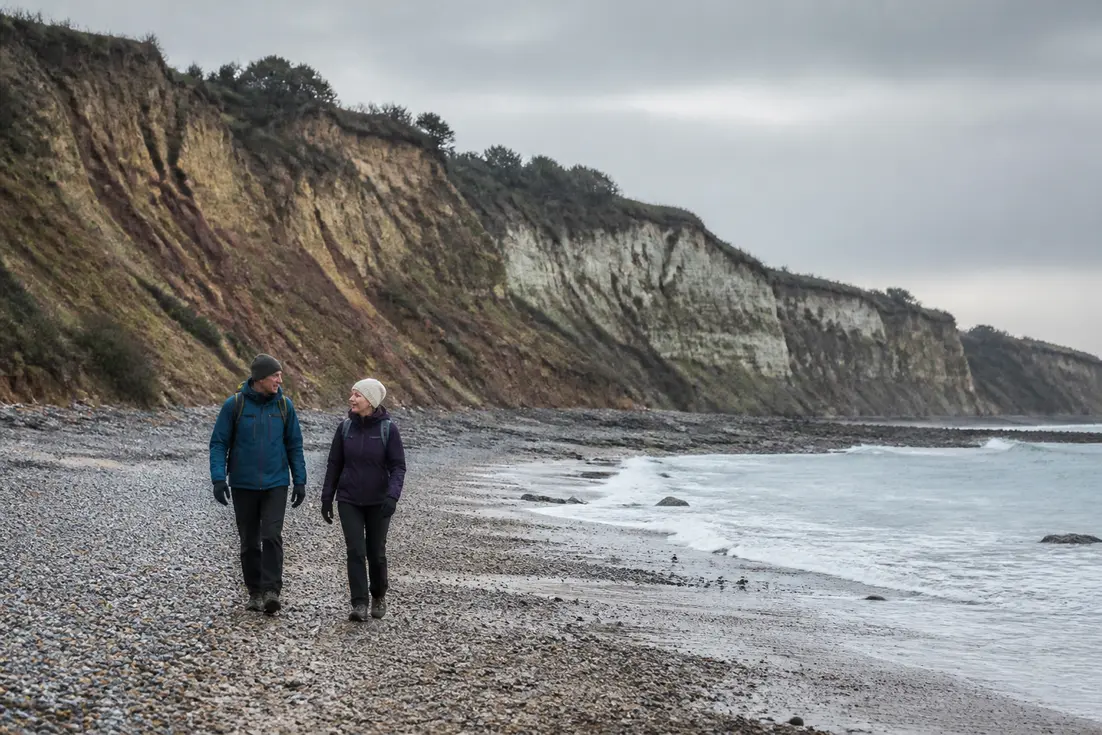 Randonneurs sur les galets pour visiter Villerville plage face aux falaises des Roches Noires.