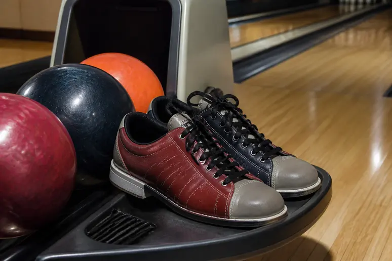Paires de chaussures et boules de bowling disposées près des pistes en bois.