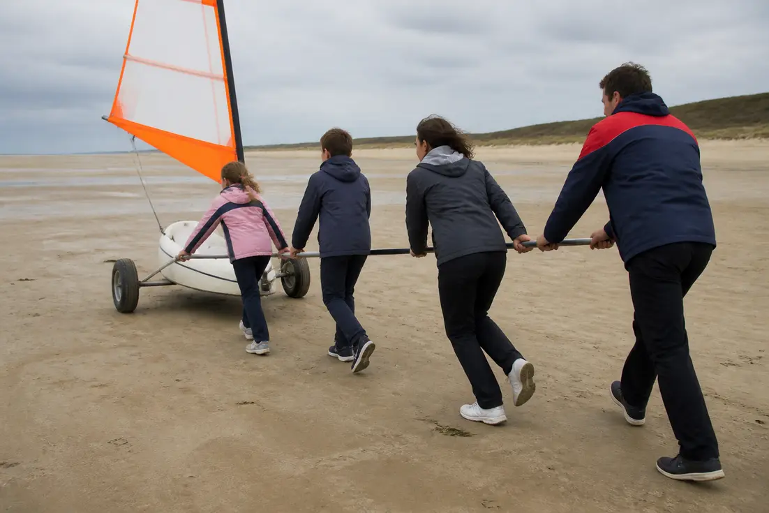 Une famille en vêtements de saison prépare son char à voile prix plages sur le sable.