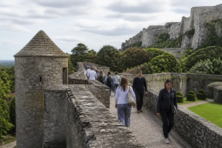 Visiteurs marchant librement sur les remparts anciens lors d'un circuit médiéval normand à petit budget