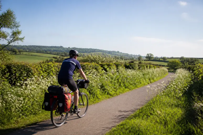 Cycliste équipé en voyage à vélo sur une piste verte traversant le bocage normand