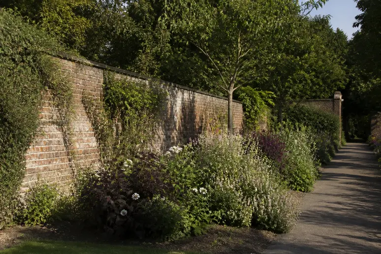 Allée bordée de murs anciens et de parterres fleuris dans les jardins clos historiques.