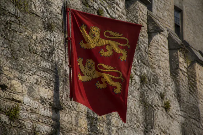 Drapeau rouge aux léopards d'or suspendu sur un mur en pierre en Normandie