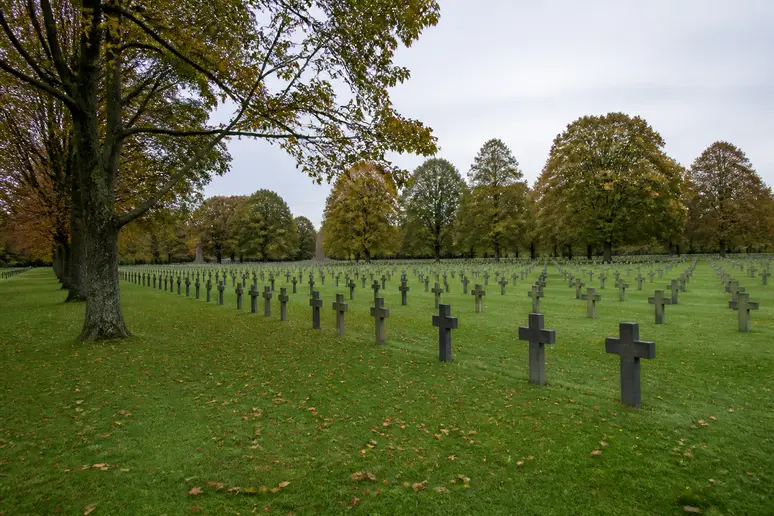 Alignement de croix funéraires en pierre sombre dans un cimetière militaire allemand en Normandie.