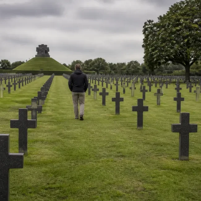 Un visiteur se recueille dans les allées d'un cimetière allemand Normandie sous un ciel nuageux.