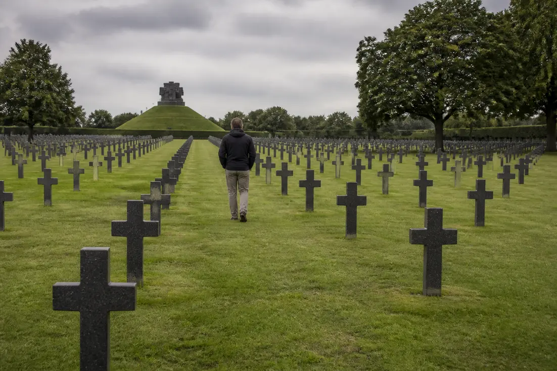 Un visiteur se recueille dans les allées d'un cimetière allemand Normandie sous un ciel nuageux.