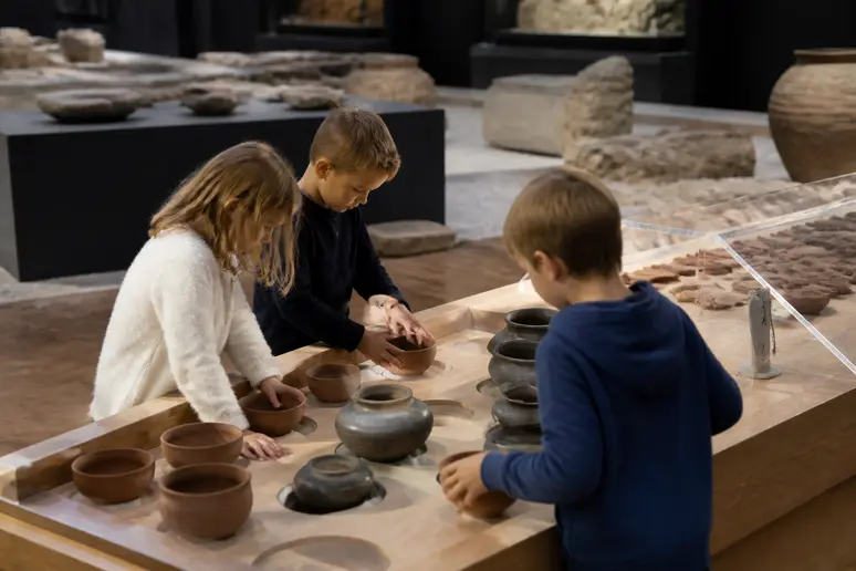 Enfants découvrant les objets gallo-romains lors d'une visite de Vieux-la-Romaine en famille.
